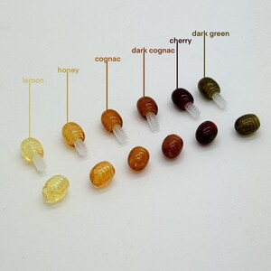 May include: Assortment of 10 amber glass beads with screw-on caps in various shades of yellow, orange, brown, and green. The beads are labeled with their color names: lemon, honey, cognac, dark cognac, cherry, and dark green.