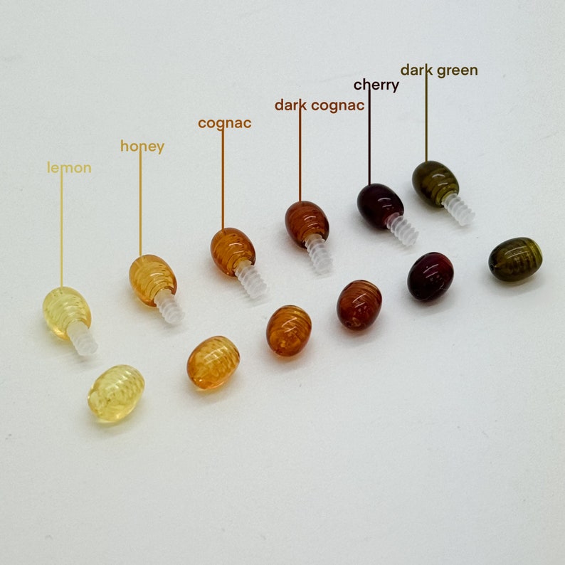 May include: Assortment of 10 amber glass beads with screw-on caps in various shades of yellow, orange, brown, and green. The beads are labeled with their color names: lemon, honey, cognac, dark cognac, cherry, and dark green.