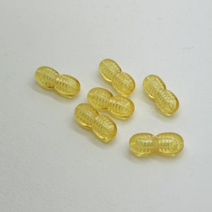 May include: Six yellow peanut-shaped beads with a textured surface. The beads are arranged in a semi-circle on a white background.