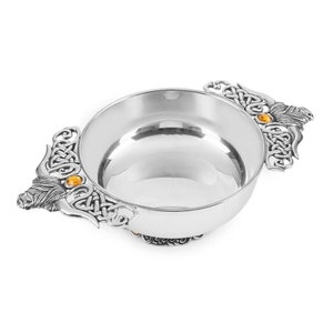 May include: A silver Celtic knotwork design drinking cup with two handles, each featuring a sculpted bull's head and an amber gemstone.