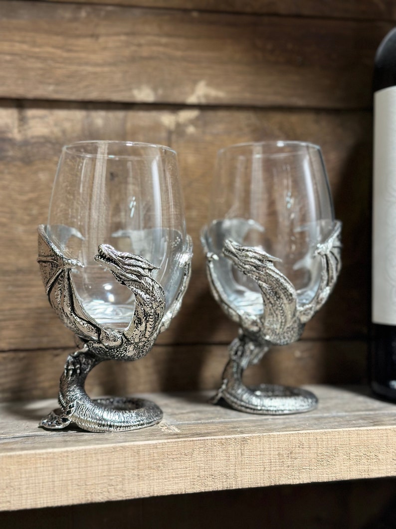 May include: Two silver dragon wine glasses with clear glass goblets. The dragon's wings and tail form the base of the glass.