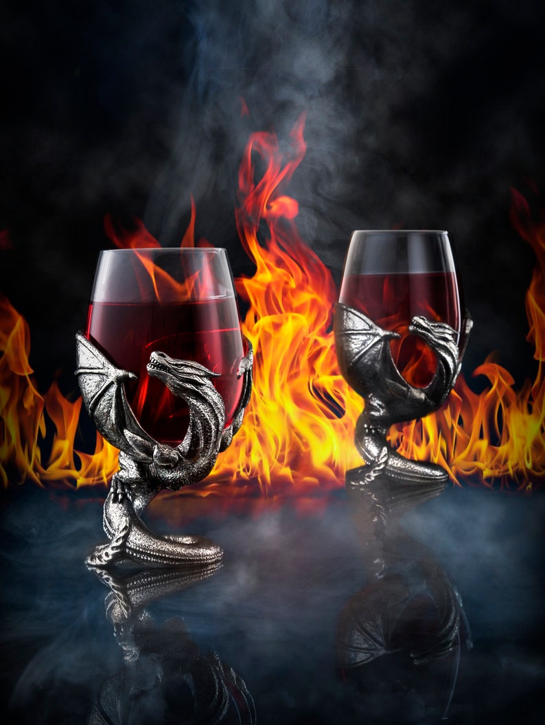 May include: Two silver dragon goblets filled with red wine, set against a backdrop of flames and smoke.