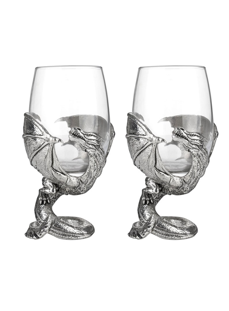 May include: Two silver dragon wine glass holders with clear glass wine glasses. The dragons are curled around the base of the glasses, with their wings outstretched.