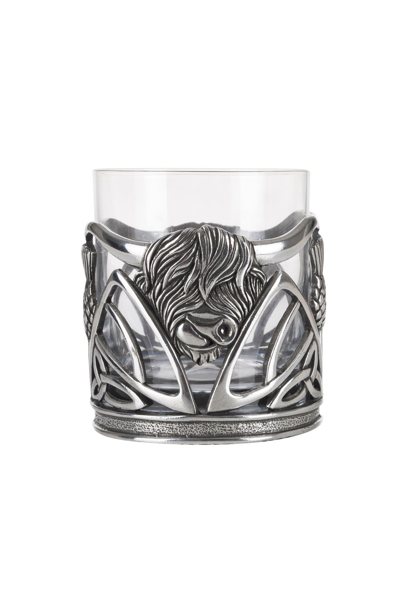 May include: A silver Highland Cow design whisky glass with a Celtic knot pattern. The glass is clear and has a silver rim.