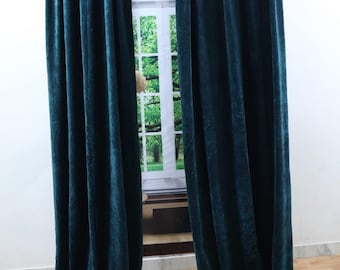 Puede incluir: Dos cortinas de terciopelo azul verdoso colgadas delante de una ventana. Las cortinas están completamente extendidas y llegan al suelo.