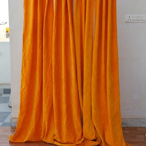 May include: A set of orange velvet curtains hanging from a rod. The curtains are gathered at the top and have a smooth, luxurious texture.