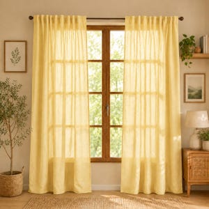 May include: A pair of floor-length, semi-sheer curtains in a soft yellow hue, featuring a pleated top header suspended from a dark metal rod. The fabric has a visible, slightly textured weave that allows natural light to filter through the panels.