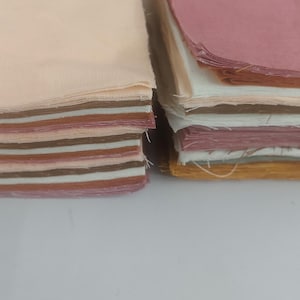 May include: Two stacks of fabric squares in various colors. The left stack features shades of beige, brown, and pink. The right stack includes pink, white, and yellow-brown hues. The fabric appears to be cotton or a similar material, suitable for quilting or crafting.