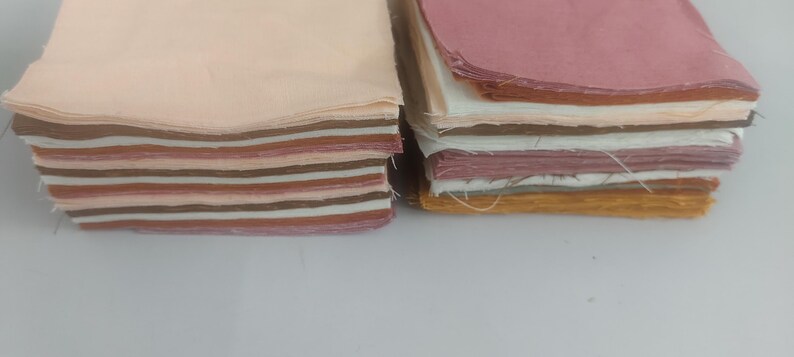 May include: Two stacks of fabric squares in various colors. The left stack features shades of beige, brown, and pink. The right stack includes pink, white, and yellow-brown hues. The fabric appears to be cotton or a similar material, suitable for quilting or crafting.