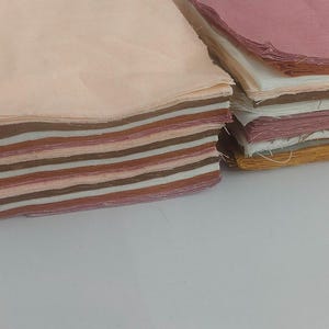 May include: Two stacks of fabric squares in various shades of pink, brown, and cream. The squares are neatly stacked, showcasing the different colors and textures of the fabric. The fabric appears to be cotton or a similar material.