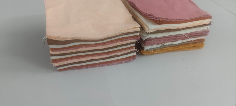 May include: Two stacks of fabric squares in various shades of pink, brown, and cream. The squares are neatly stacked, showcasing the different colors and textures of the fabric. The fabric appears to be cotton or a similar material.