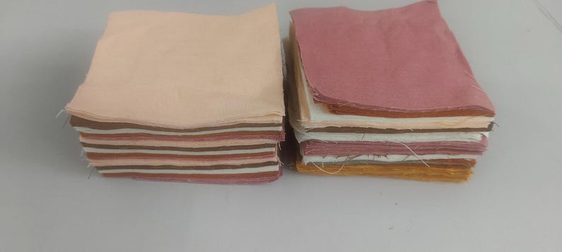 May include: Two stacks of fabric squares in various colors. One stack features a light peach color on top, with stripes of brown, pink, and cream underneath. The other stack has a pink top layer, with layers of white, orange, and yellow visible.