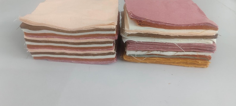 May include: Two stacks of fabric squares in various shades of pink, brown, and cream. The fabric appears to be cotton or a similar material, with visible edges. The stacks are arranged side by side on a white surface, suggesting a craft or sewing project.