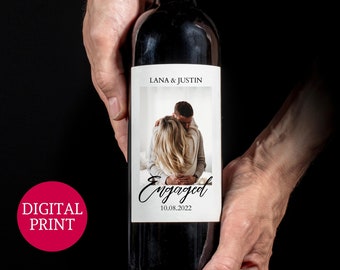 May include: A red wine bottle with a personalised label. The label features a photo of a couple embracing, the text "Lana & Justin", and the words "Engaged 10.08.2022".