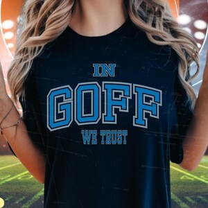 May include: A dark blue t-shirt with the text "In Goff We Trust" in white and blue lettering.