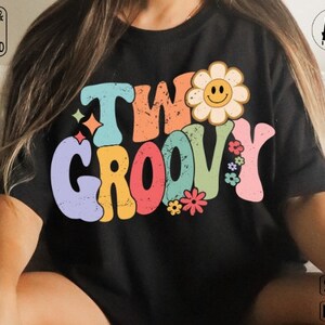 May include: A black t-shirt with a colorful retro design that says "Two Groovy" with a yellow flower with a smiley face in the center.