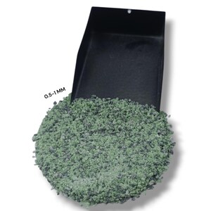 May include: A black scoop is filled with green gravel, with the text "0.5-1 MM" visible. The gravel is a mix of green and gray, and the scoop is angled to show the contents.