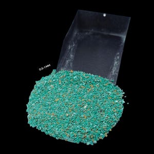 May include: A close-up of a pile of turquoise green and brown mineral chips, ranging in size from 0.5 to 1 mm, spilling out of a clear plastic scoop. The scoop is labelled "0.5-1 MM".