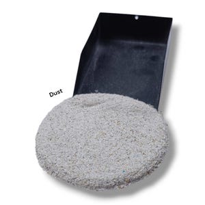 Puede incluir: Un recogedor negro lleno de un montón circular de polvo gris claro. La palabra "Dust" está impresa en negro en el recogedor. El polvo parece estar hecho de pequeñas partículas granulares.