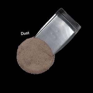 Puede incluir: Una pequeña pala de metal llena de un montón de polvo marrón. El texto "Dust" está escrito encima de la pala.