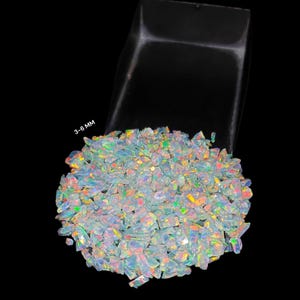 May include: A pile of iridescent opal chips in various sizes, ranging from 3-6 mm. The chips are a mix of white, blue, green, and orange.