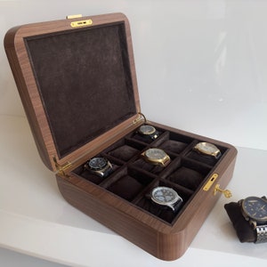 Puede incluir: Una caja de madera para relojes con un interior de terciopelo marrón y ocho compartimentos para guardar relojes. La caja tiene una cerradura y una llave de latón.