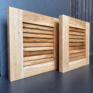 Op de afbeelding: Twee houten luiken met een lamellenontwerp. De luiken zijn gemaakt van lichtbruin hout en hebben een natuurlijke afwerking.