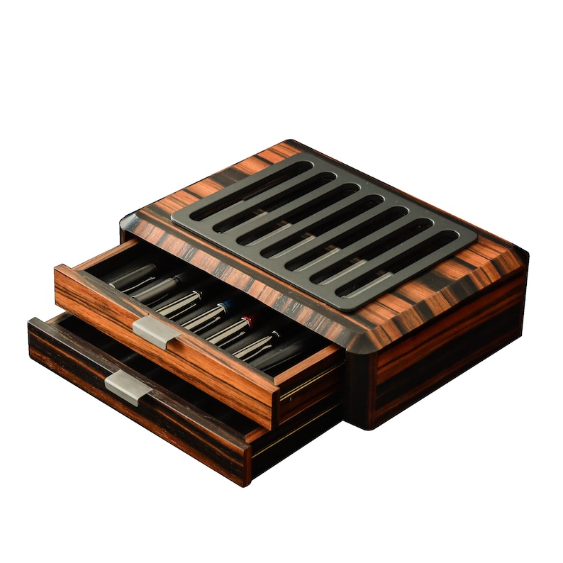 May include: A rectangular wooden storage box with a dark brown and black striped grain pattern. The box features two pull-out drawers with silver-toned metal handles and a black top panel with six parallel rectangular ventilation slots.