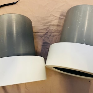 以下が含まれることがあります： 白い土台が付いた灰色の円筒形の物体2つ。物体は滑らかでわずかにざらざらした素材でできています。土台は平らで円形です。