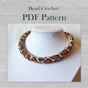 May include: A beaded crochet necklace with a pattern of black, gold, and white beads. The necklace is displayed on a white mannequin bust. The image includes the text "Bead Crochet PDF Pattern".