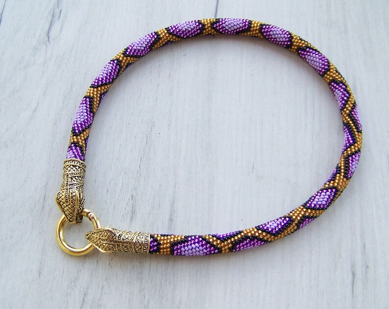 May include: A purple and gold beaded necklace with a snake-like pattern and gold metal clasps.