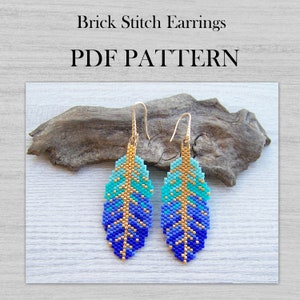 以下が含まれることがあります： ブリックステッチのイヤリングPDFパターン。 金色のフックが付いた、ビーズで作られた羽根のイヤリングが2つ。 イヤリングは、青とターコイズのグラデーションビーズと金色のアクセントが特徴です。 流木の上にイヤリングが飾られています。