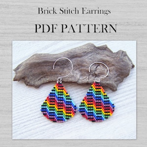 Può includere: Un paio di orecchini a forma di goccia realizzati con perline a punto mattoncino in colori arcobaleno. Gli orecchini sono appesi a ganci per orecchie argentati. Gli orecchini sono su un pezzo di legno di deriva. Il testo "PDF PATTERN" è scritto in lettere nere su sfondo bianco.