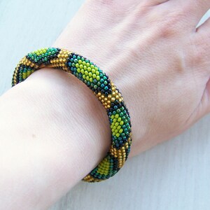 May include: A green, gold, and black beaded bracelet with a geometric pattern.