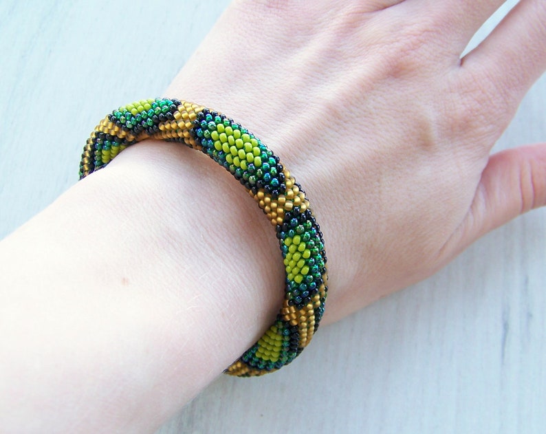 May include: A green, gold, and black beaded bracelet with a geometric pattern.