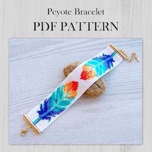 Może przedstawiać: Biała bransoletka w technice peyote z kolorowym wzorem piór. Bransoletka jest wykonana z koralików i ma złoty zamek. Bransoletka leży na drewnianej powierzchni. PDF PATTERN
