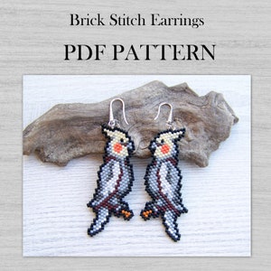 May include: A pair of brick stitch earrings featuring a gray and white cockatiel design. The earrings are made with seed beads and have silver ear wires. The earrings are displayed on a piece of driftwood. PDF PATTERN.