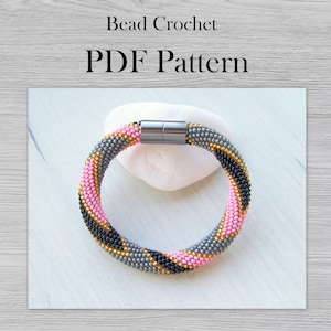 May include: A beaded bracelet with a magnetic clasp. The bracelet is made with gray, pink, black, and gold beads. The bracelet is on a white background.