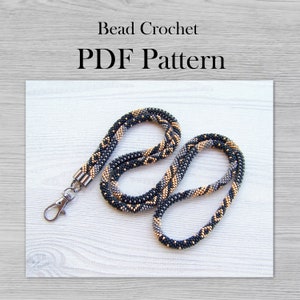 Op de afbeelding: Een zwart, grijs en gouden kralenkoord met een zilveren sluiting. Kralenbreien PDF-patroon.