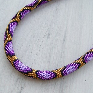 May include: A purple, gold, and black beaded necklace with a snake skin pattern.