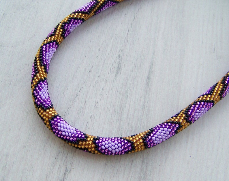 May include: A purple, gold, and black beaded necklace with a snake skin pattern.