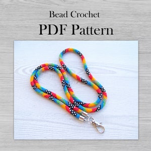 May include: A colourful beaded lanyard with a silver clasp. The lanyard is made with red, orange, yellow, green, blue, black, and silver beads. Bead Crochet PDF Pattern.