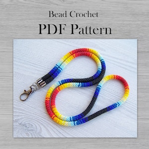 May include: A colorful beaded lanyard with a red, yellow, white, blue, and black color gradient. The lanyard has a silver clasp and is made with small beads. Bead Crochet PDF Pattern.