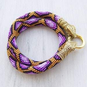 May include: A purple and gold beaded necklace with a geometric pattern and gold metal clasps.