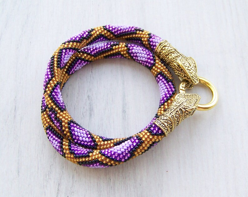 May include: A purple and gold beaded necklace with a geometric pattern and gold metal clasps.