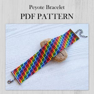 Può includere: Un braccialetto colorato a punto peyote con un motivo arcobaleno. Il braccialetto ha una chiusura argentata e una chiusura a scorrimento argentata. MODELLO PDF.