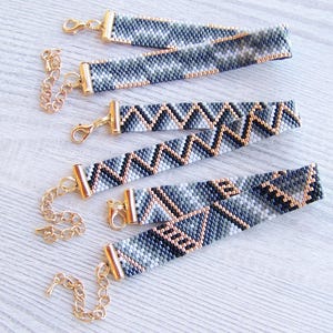 May include: Four beaded bracelets with geometric patterns in shades of gray, black, and gold. The bracelets have gold clasps and are strung on a gold chain.