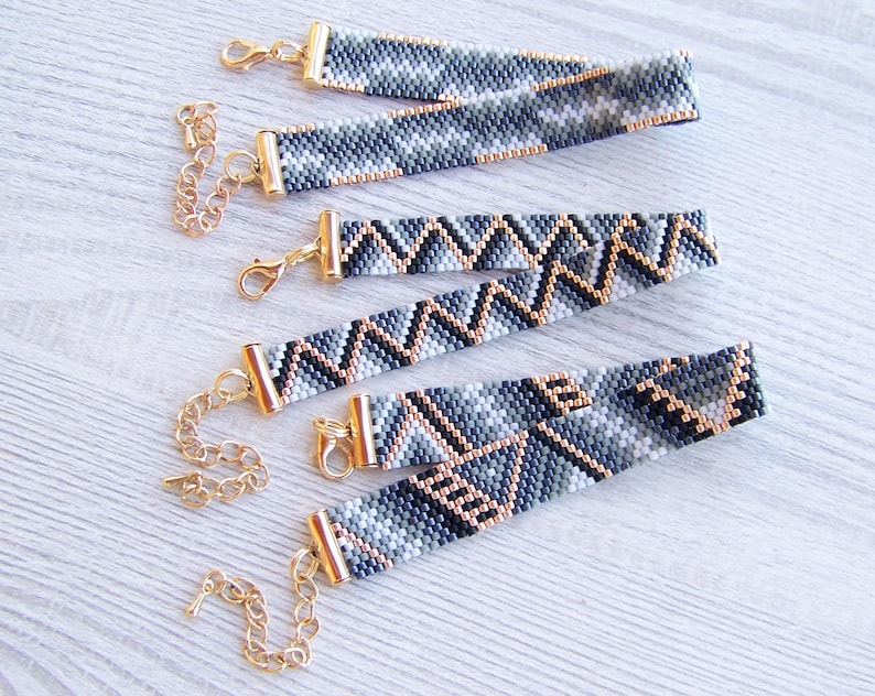 May include: Four beaded bracelets with geometric patterns in shades of gray, black, and gold. The bracelets have gold clasps and are strung on a gold chain.