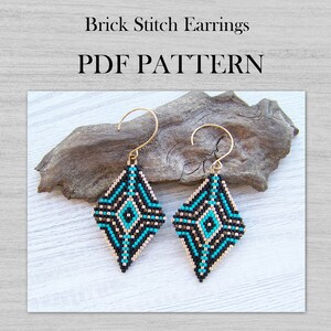 Puede incluir: Un par de pendientes de cuentas turquesa, negro y dorado con forma de diamante geométrico. Los pendientes están hechos con punto de ladrillo y tienen ganchos dorados. Los pendientes se muestran en un trozo de madera flotante. PDF PATTERN.