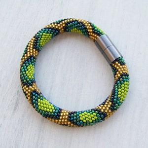 May include: A green, gold, and black beaded bracelet with a magnetic clasp.